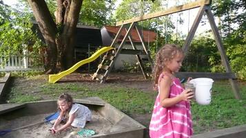 Des enfants jouent dans un bac à sable, avec un portique et un toboggan en arrière-plan.