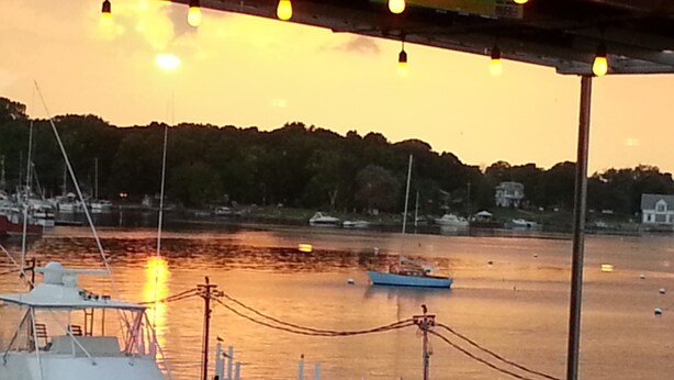 En lystbådehavn med fortøjede både, en solnedgang i baggrunden og en person ved vandet.