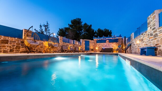 A swimming pool with stone walls and hanging chairs.