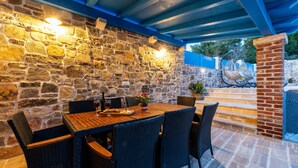 A stone wall with a wooden table and chairs, a potted plant, and a brick column.