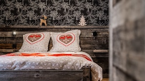 A bed with a patterned bedspread, two heart-shaped pillows, and a small Christmas tree decoration on a wooden headboard. - Charming mountain apartment (Saint-Chaffrey)