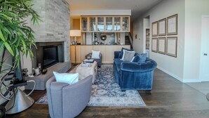 A modern living room with a fireplace, grey sofas, a blue velvet sofa, and a kitchen in the background. - Panoramic Skyline View ll Luxury Residence (Seattle)
