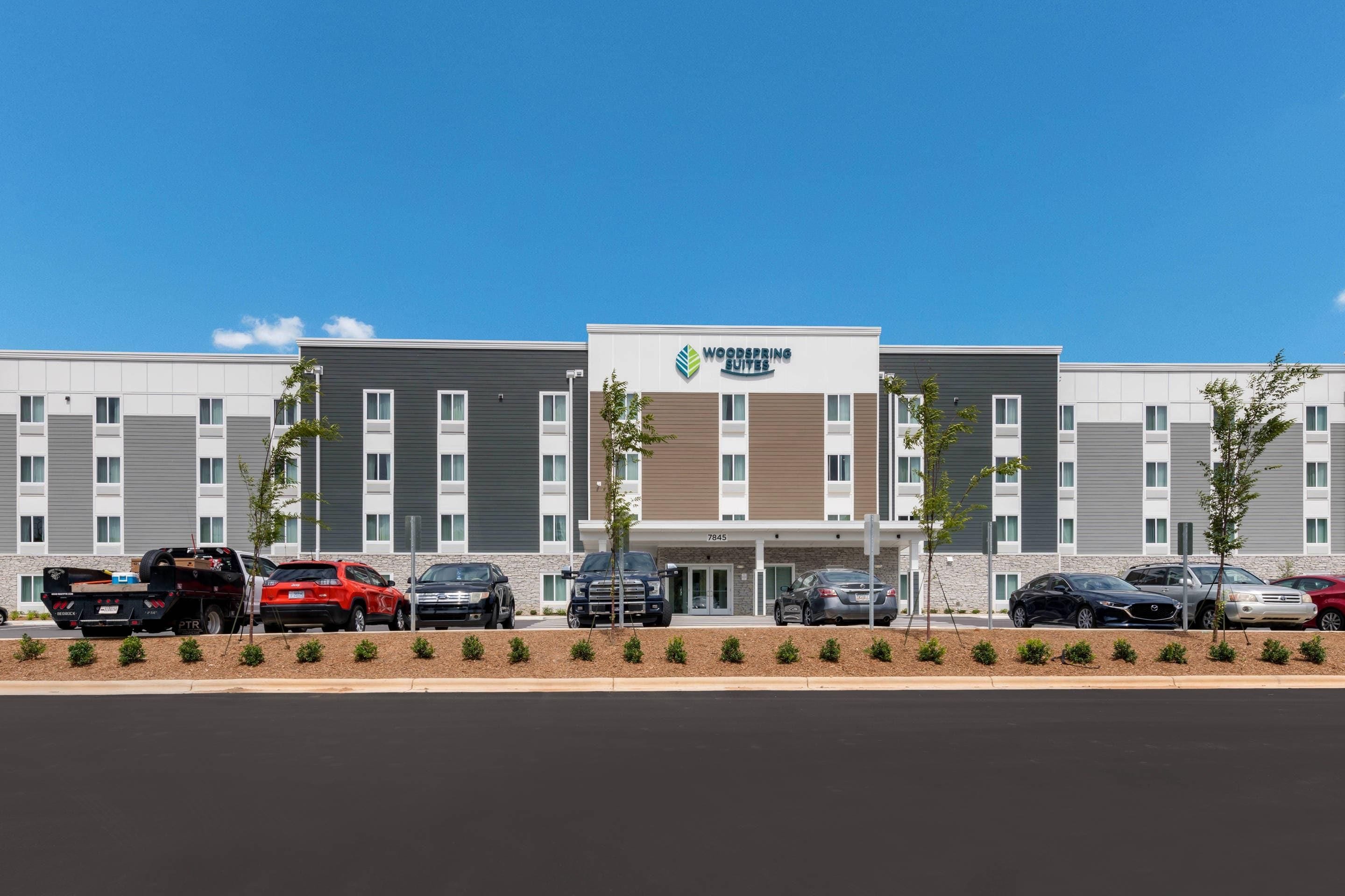 A multi-story hotel with a modern design, featuring a parking lot with several cars.