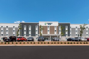 A multi-story hotel with a modern design, featuring a parking lot with several cars. - WoodSpring Suites Concord-Charlotte Speedway (Concord)