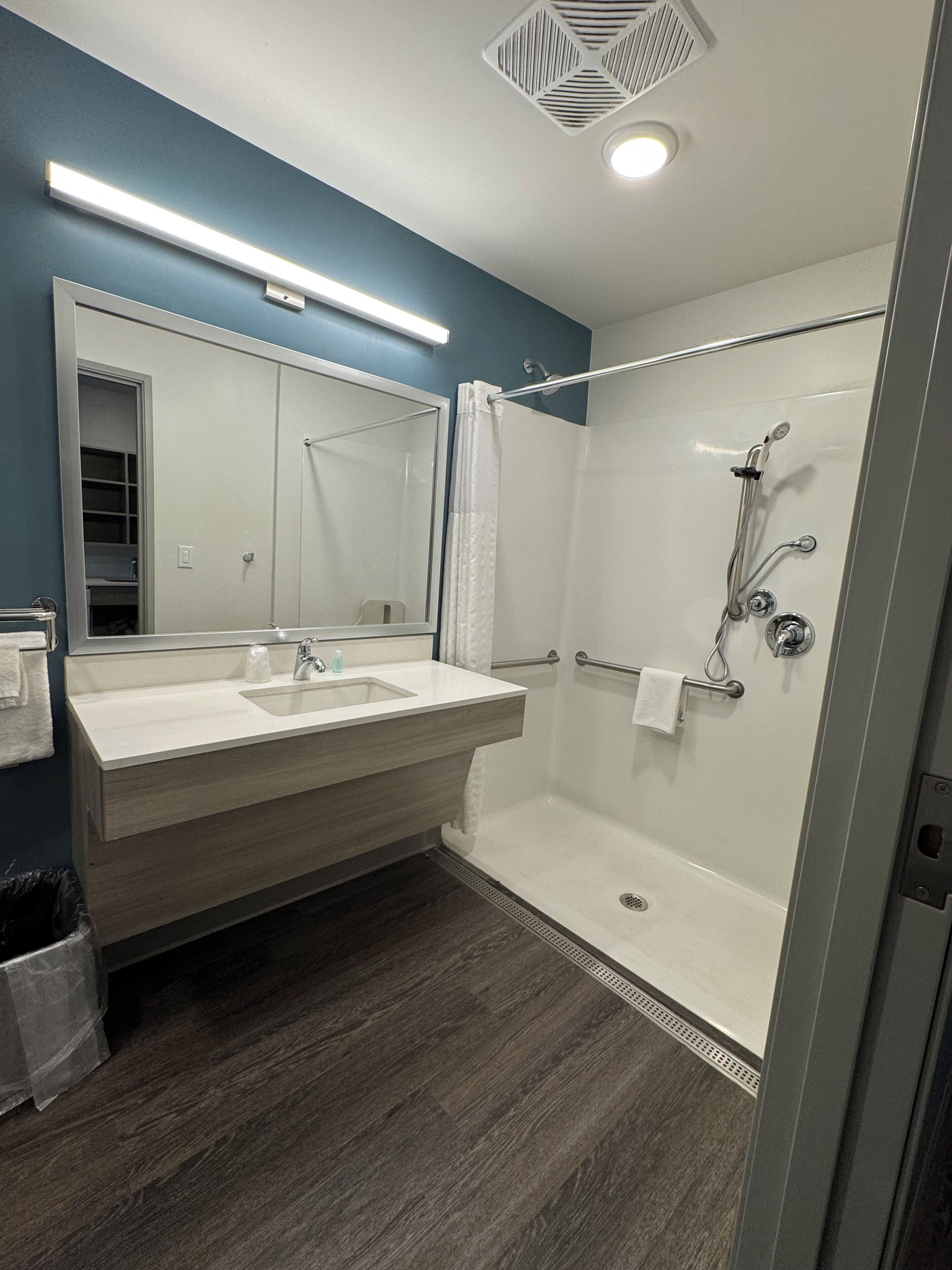 A modern bathroom with a double sink vanity, a glass shower enclosure, and a ceiling vent.