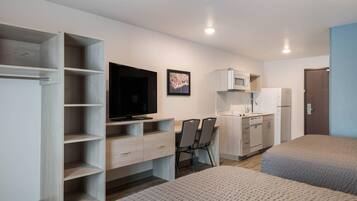 Habitación de hotel compacta con kitchenette, una cama, un escritorio con silla y televisor.