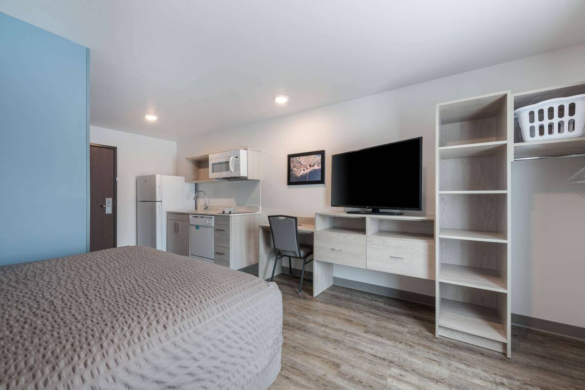 A compact hotel room with a bed, a desk with a chair, a television, a microwave, and a wardrobe.