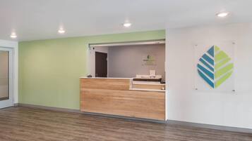 Un espace d’accueil avec un comptoir de réception en bois, un mur végétal et un logo affiché sur le mur.