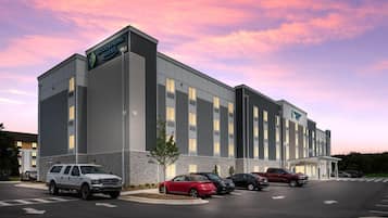 A hotel with a modern design, featuring a stone facade and multiple windows. There are several cars parked in the driveway.