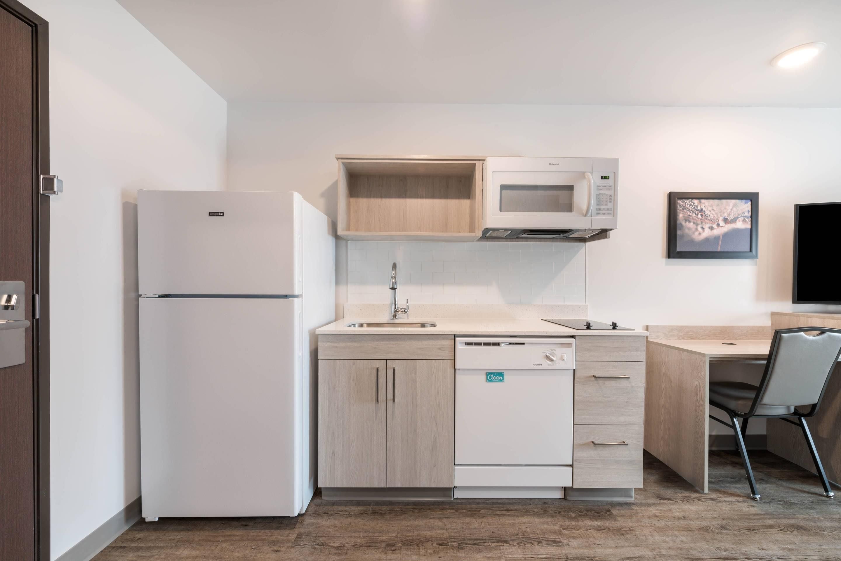 A compact kitchen with a refrigerator, microwave, dishwasher, and a small wooden cabinet.