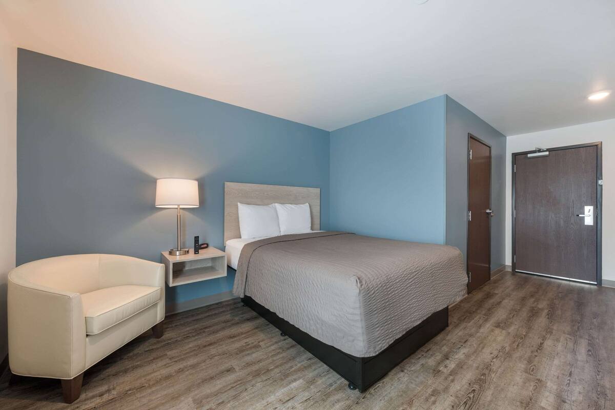 A bedroom with a bed, a chair, a nightstand, and a door.