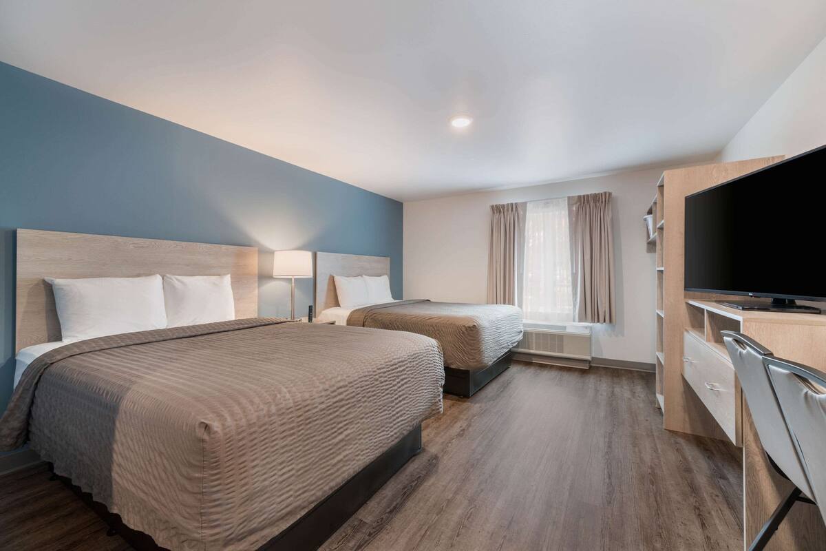 A hotel room with two beds, a TV, a desk, and a window with curtains.