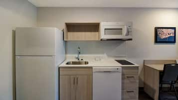 A compact kitchen with a refrigerator, microwave, sink, dishwasher, and a small dining area with a chair.