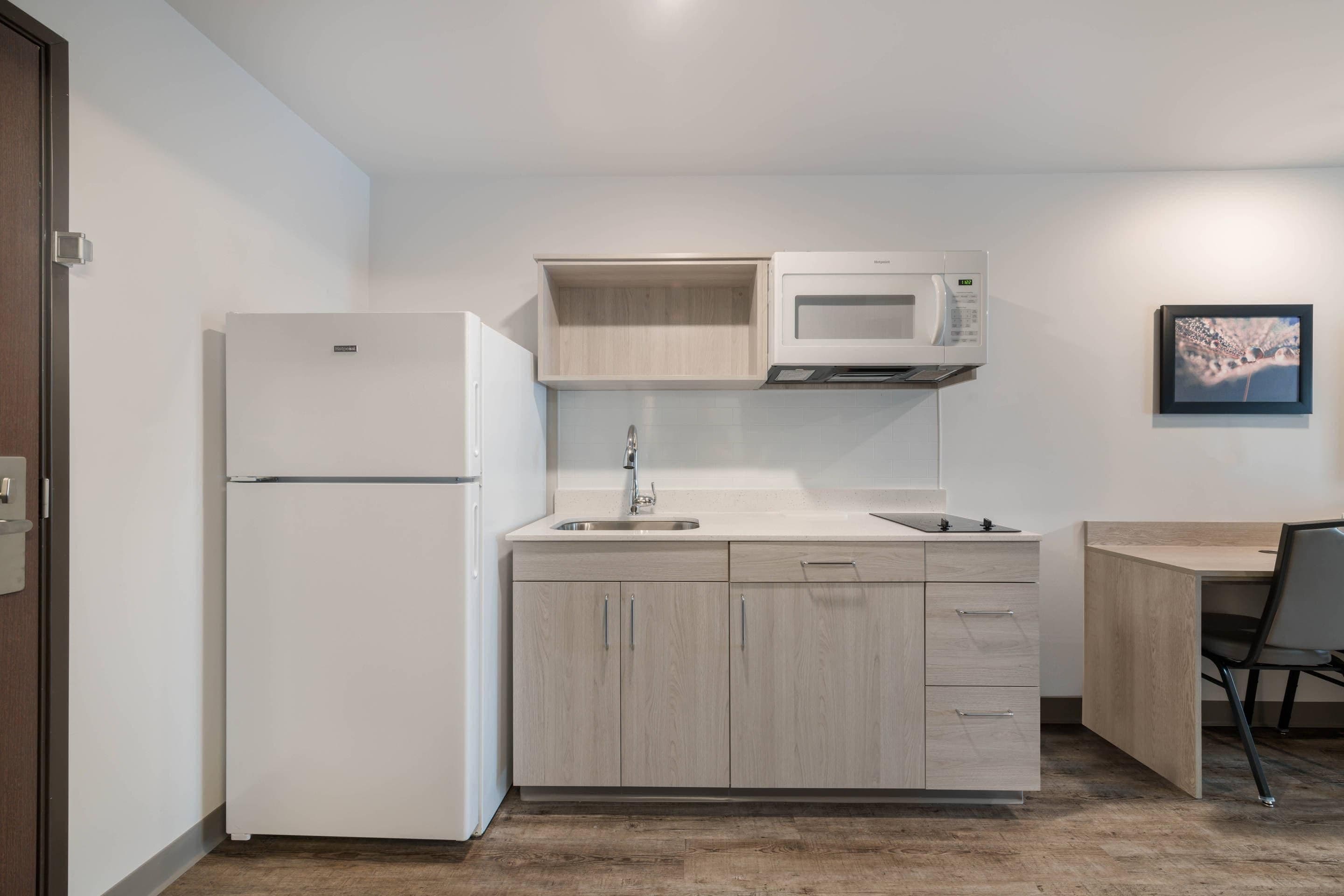 A compact kitchen with a refrigerator, microwave, sink, and wooden cabinets.
