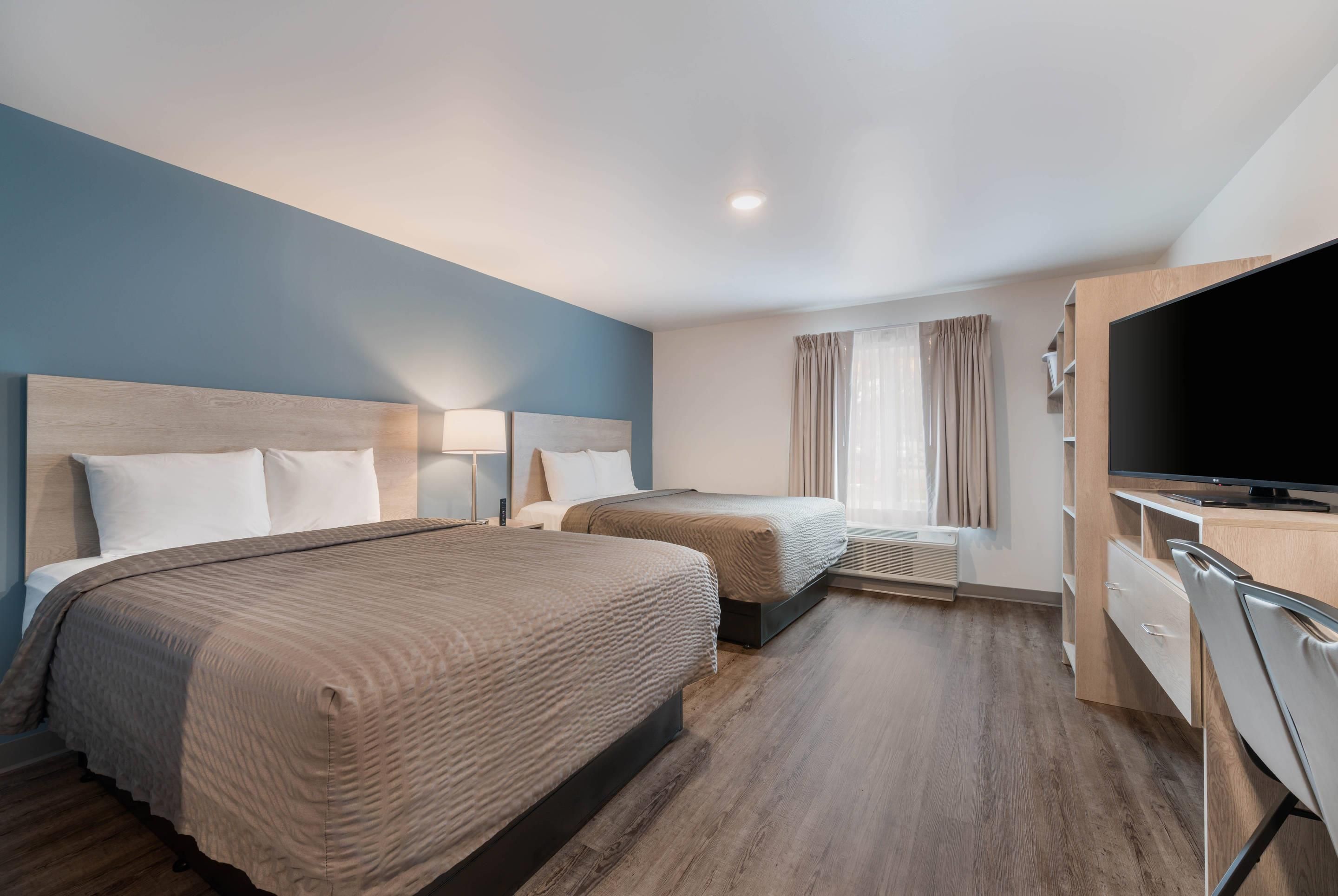 A hotel room with two beds, a TV, a desk, and a window with curtains.