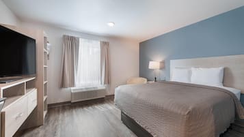 Habitación de hotel con cama, televisión, escritorio, silla, lámpara y ventana con cortinas.