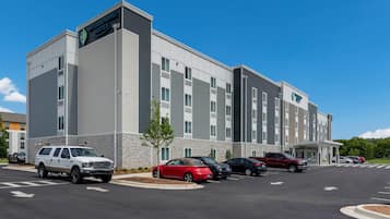 A multi-story hotel with a modern design, featuring a stone facade and a parking lot with several cars.