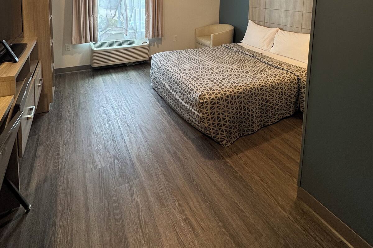 A hotel room with a bed, a chair, a desk with a computer, and a window with curtains.