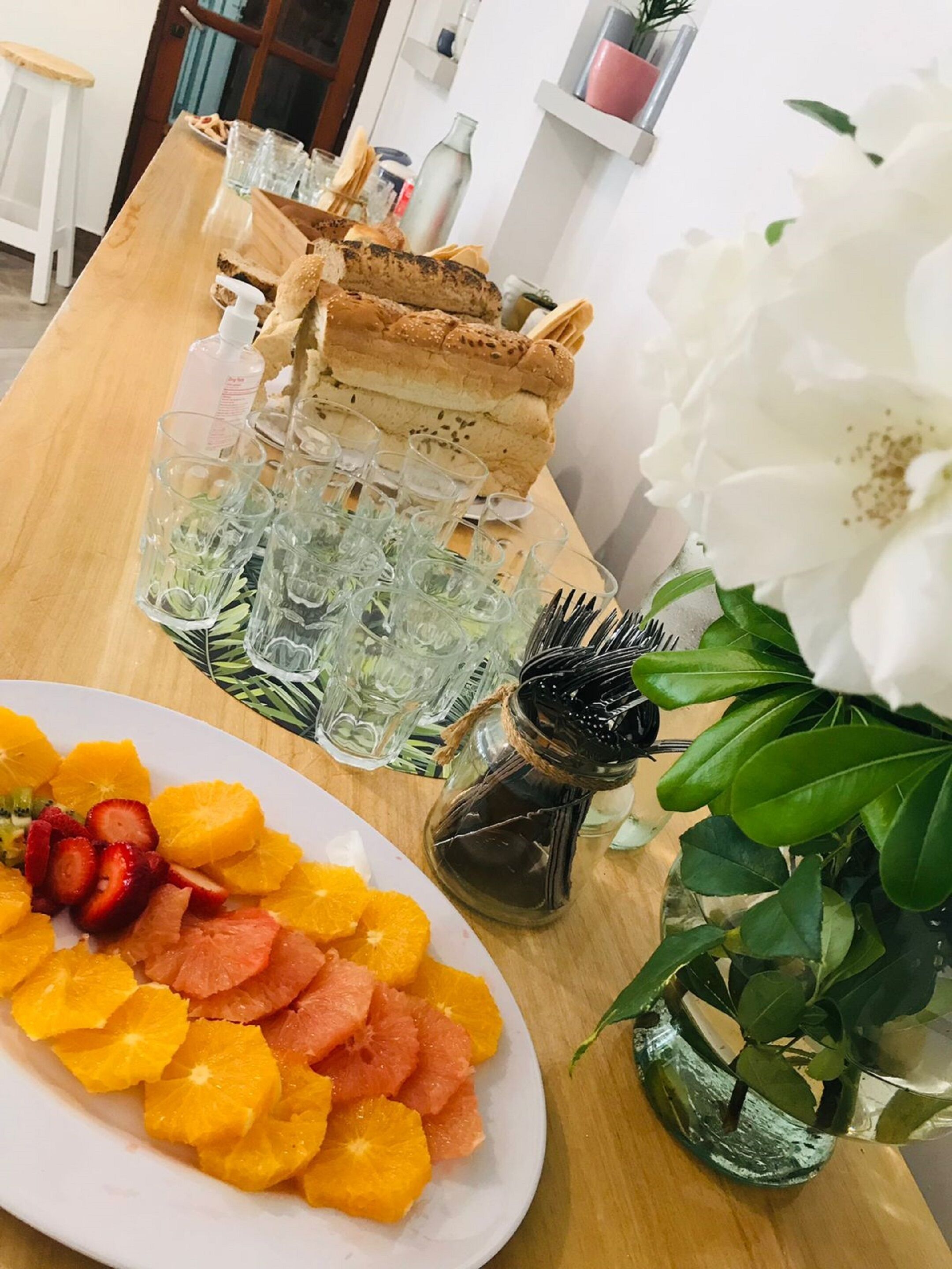 Une table en bois sur laquelle se trouvent une assiette de fruits, une bouteille de sauce et un pichet en verre.