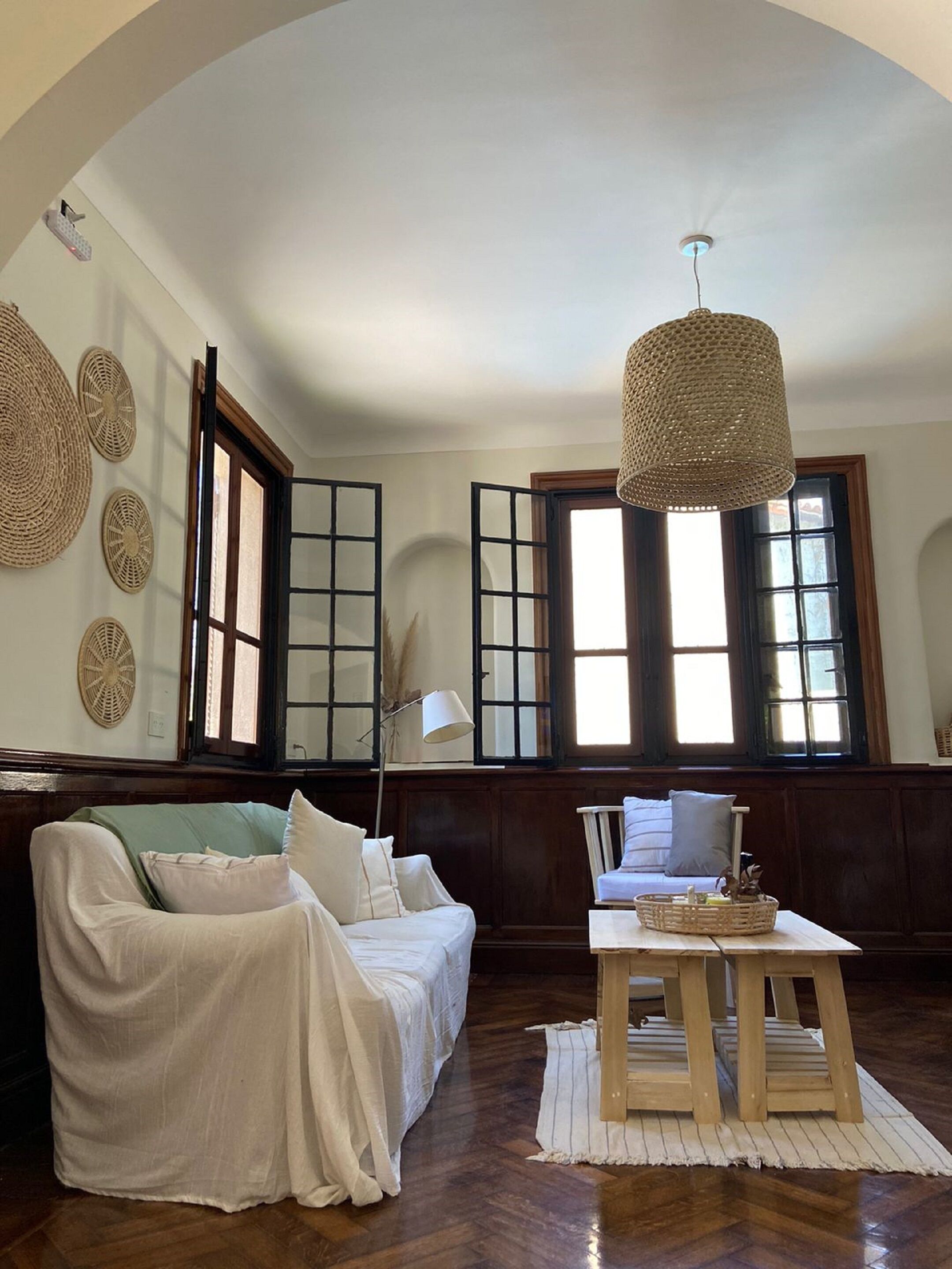 Een woonkamer met een hoge gewelfde plafond, een bank, een tafel en grote ramen met veel ruitjes.