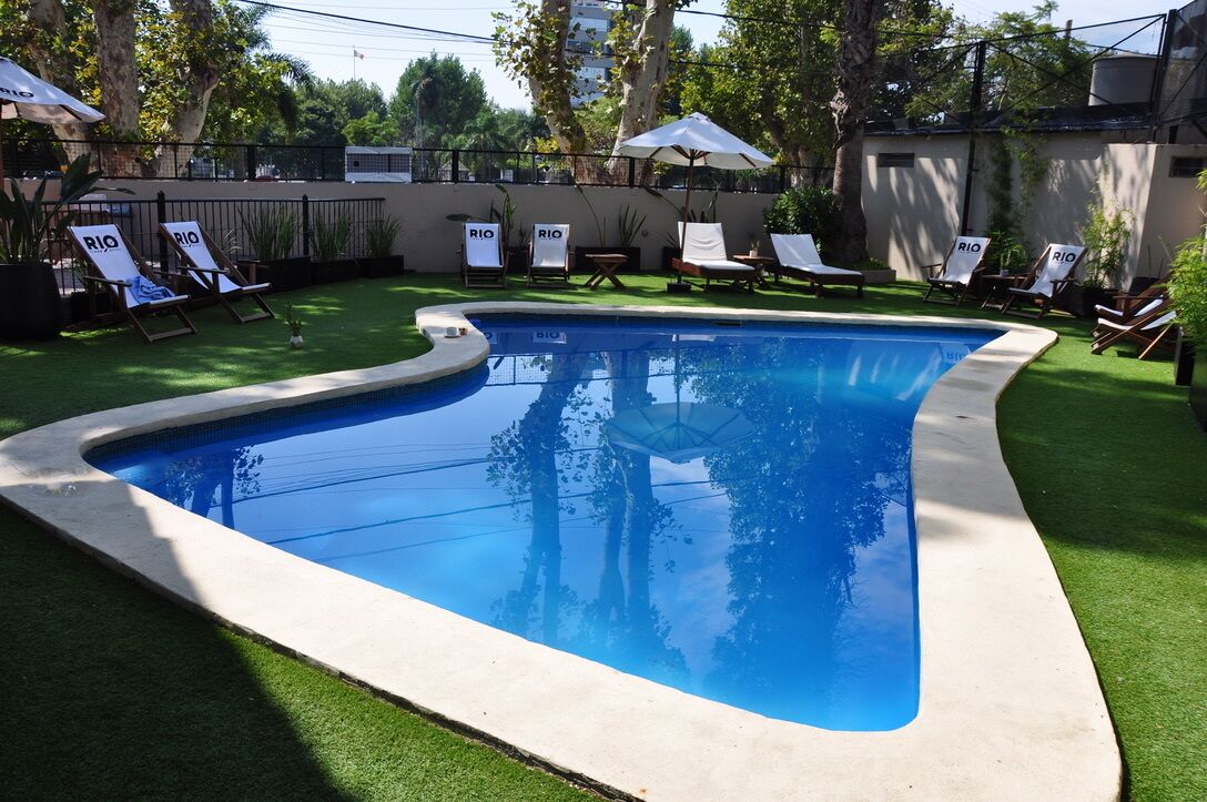 Una piscina de borde curvo, rodeada de césped artificial y sillas de descanso.