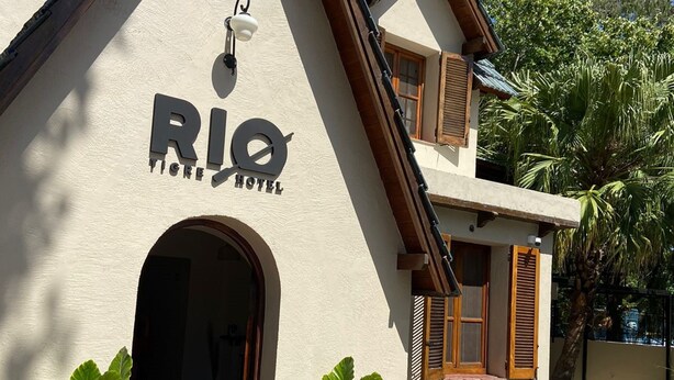 Un hotel llamado "Rio Tigre Hotel" con una entrada destacada, plantas en macetas y una vista despejada del entorno.
