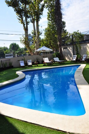 A swimming pool with a curved edge, surrounded by a grassy area and trees. There are lounge chairs with "RIO" signs, and a white umbrella. - Rio Tigre Hotel (Tigre)