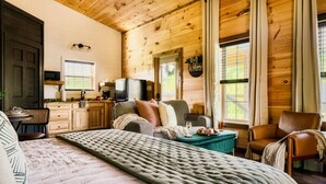 A cozy cabin-style room with a large bed, a sofa, a dining table, and a kitchen area.
