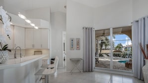 Eine moderne Küche mit weißen Schränken, einer Bar und Blick auf einen Pool durch große Glastüren.