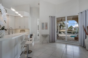A modern kitchen with white cabinets, a bar area, and a view of a pool through large glass doors. -  VILLA BELLAGGIO - Western Exposure, Gulf Access, Pool, Boatlift, 3 bed & 3 bath (Cape Coral)