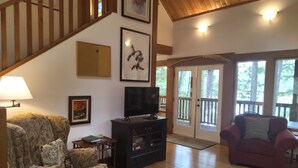A spacious living room with a wooden staircase, a television on a black entertainment unit, and a red armchair. - The Cabin at Moon Dance (Madeira Park)