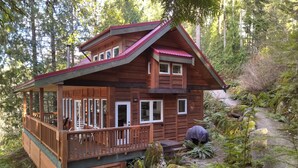 A wooden cabin with a balcony, surrounded by dense forest. - The Cabin at Moon Dance (Madeira Park)