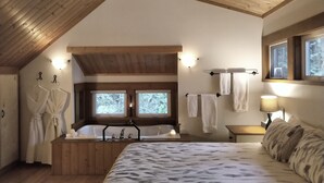 A bedroom with a wooden ceiling, a large bed, a wooden bathtub, two windows, and a nightstand with a lamp. - The Cabin at Moon Dance (Madeira Park)
