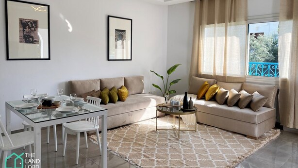 Un salon moderne avec une table à manger en verre, des canapés beige et une grande fenêtre agrémentée de rideaux.