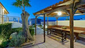 A wooden pergola with a bench, a palm tree, and a view of the sea. - Cozy Vintage Style Apartment Shared Pool RU (Malevizi)