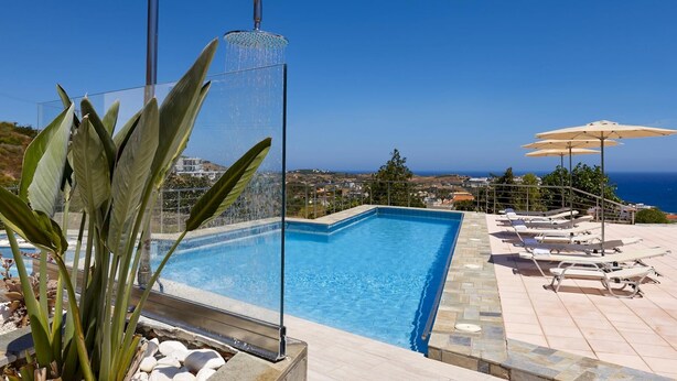 A swimming pool with a waterfall feature, surrounded by lounge chairs and umbrellas, overlooking a coastal landscape. - Cozy Vintage Style Apartment Shared Pool RU (Malevizi)
