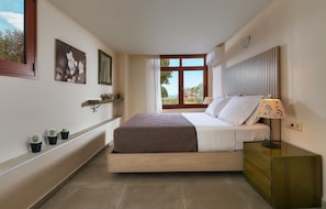 A bedroom with a bed, bedside table, lamp, and a window with a view.