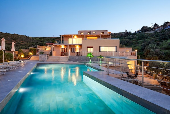 A modern hotel with a swimming pool, outdoor seating, and a hillside view.