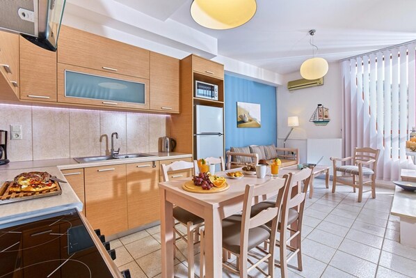 A modern kitchen with wooden cabinets, a built-in oven, and a dining area with a table and chairs. - Bright Family Apartment With Shared Pool RU (Malevizi)