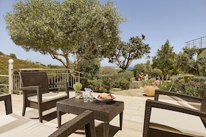 An outdoor patio with wicker furniture, a bowl of fruit, and a pitcher of water.