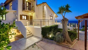 Una casa de dos pisos con balcón, una escalera y un jardín bien cuidado con una palmera.