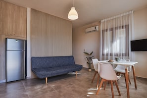 A modern kitchen with a built-in refrigerator, a blue sofa, a dining table with chairs, and a potted plant.