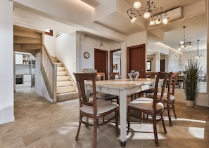 A spacious dining area with a wooden table and chairs, a staircase leading to a kitchen, and a large mirror reflecting the room.