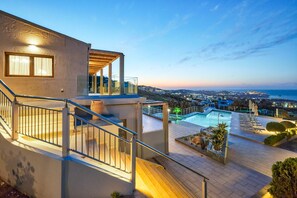 A modern building with a pool, outdoor seating, and a view of the sea.