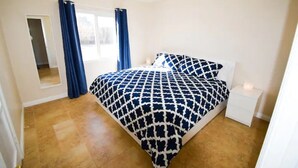 A bedroom with a bed, a nightstand, a window with curtains, and a door.