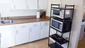 A kitchen with white cabinets, a granite countertop, a black metal rack with appliances, and a tiled floor.