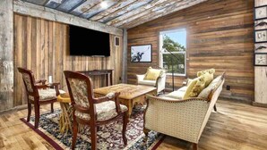 A rustic interior with wooden walls, a flat-screen TV, a dining table with chairs, and a sofa. - The Sanctuary at Fredericksburg (Gillespie County)