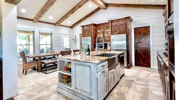 A kitchen with a large island, wooden cabinets, and a stone floor. - The Sanctuary at Fredericksburg (Gillespie County)