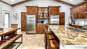 A kitchen with wooden cabinets, a stone floor, and a granite countertop. - The Sanctuary at Fredericksburg (Gillespie County)