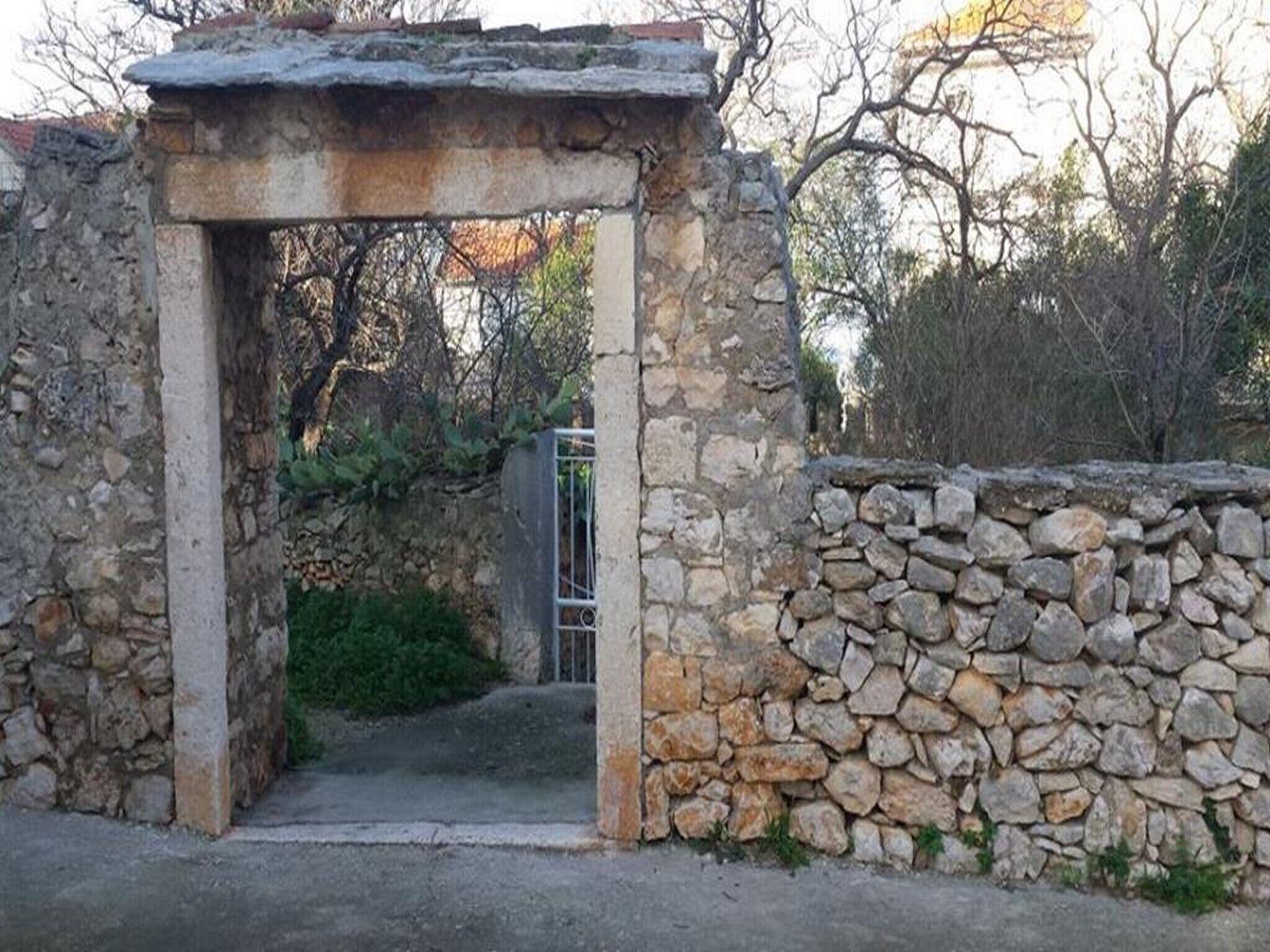 A stone archway leading to a courtyard with a stone wall and greenery.